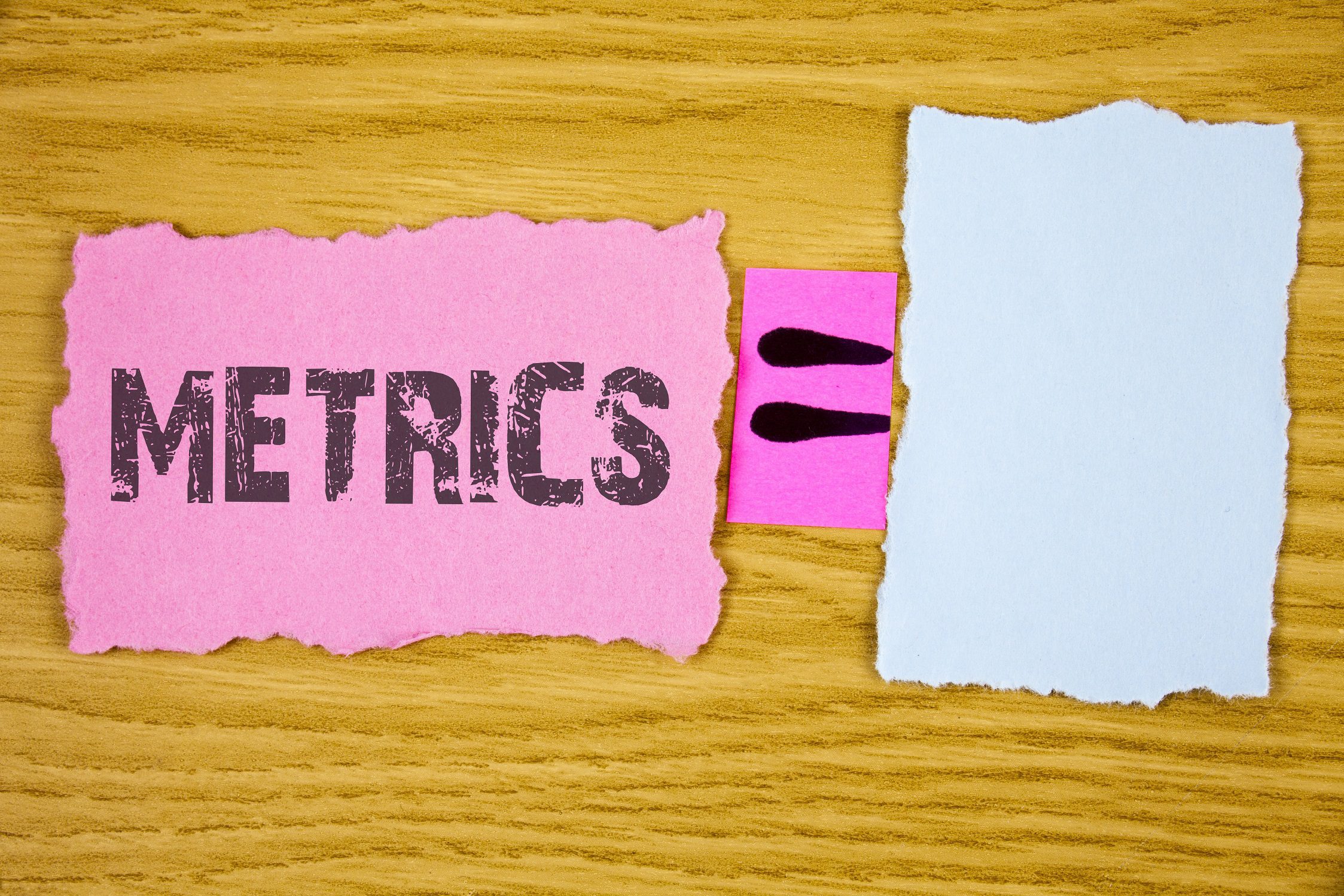 word "metrics" written on pink piece of paper, with a smaller paper that has the "equals" sign, and a third blank white piece of paper