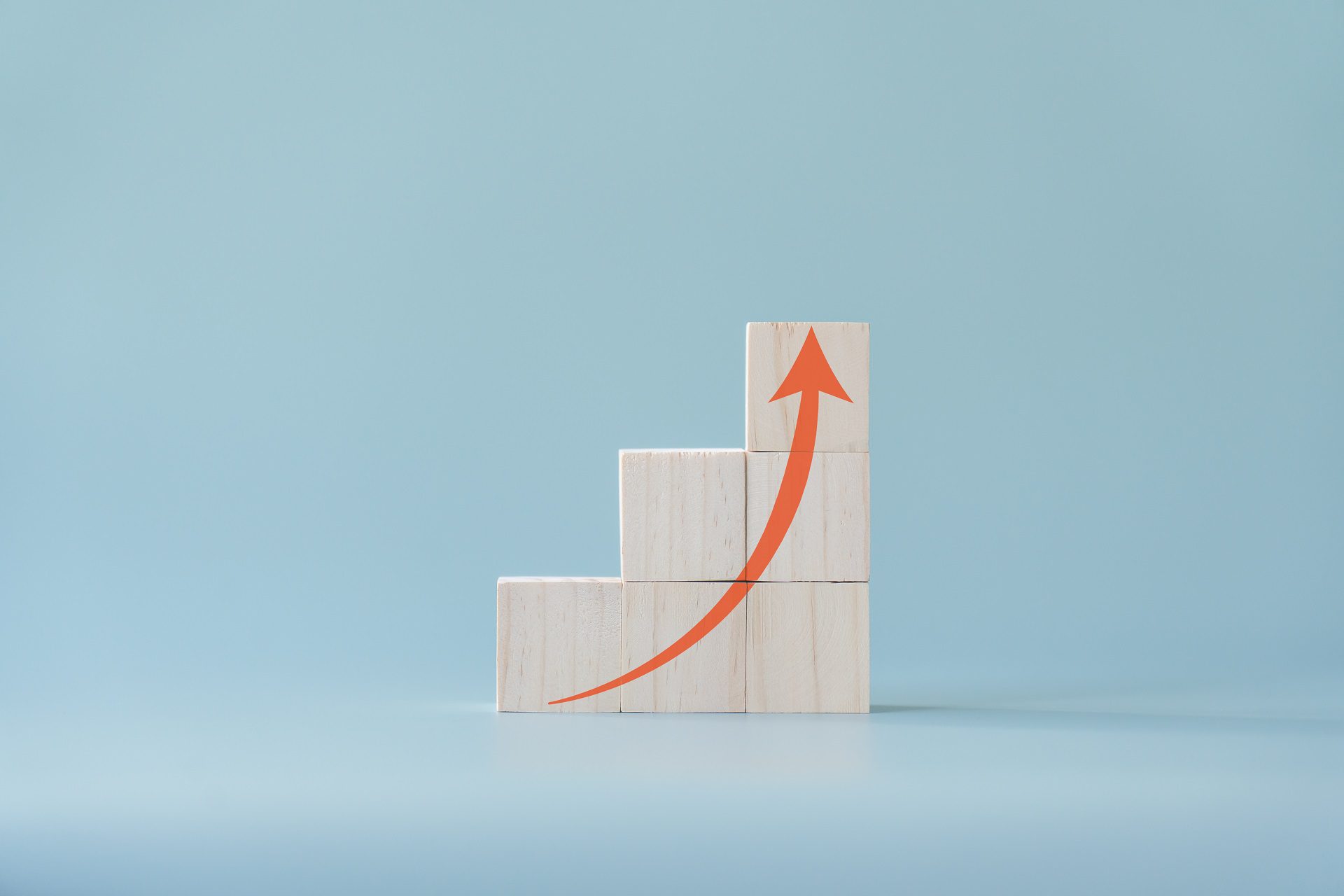 Red arrow going up on wooden blocks and light blue background. Concept of growing or improving.